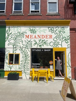 Meander's botanical storefront in downtown Elkins with Rosalie Haizlett standing in the open yellow doorway