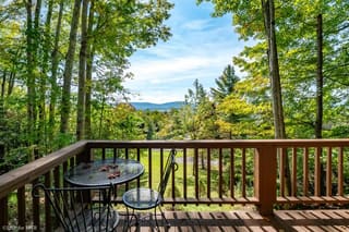 Lower deck with Adirondack chairs and view towards mountains in summer